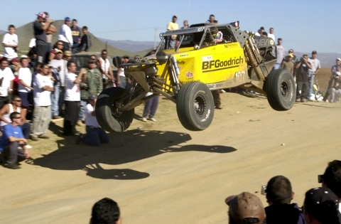 BFGoodrich Offroad vehicle in air on dirt road during Baja 1000 Off-Road Race, spectators both sides